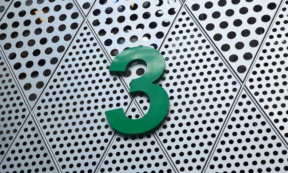 a green number 3 on a metal wall representing 3 in Numerology
